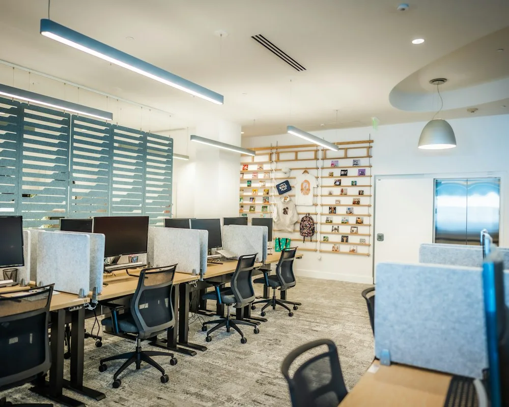 Escritório iluminado com estações de trabalho, mesas e cadeiras.