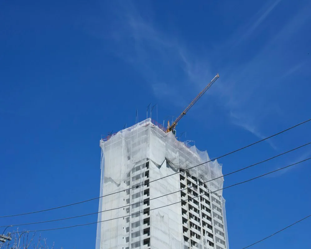 Edifício em construção com uma grua sob o céu azul.
