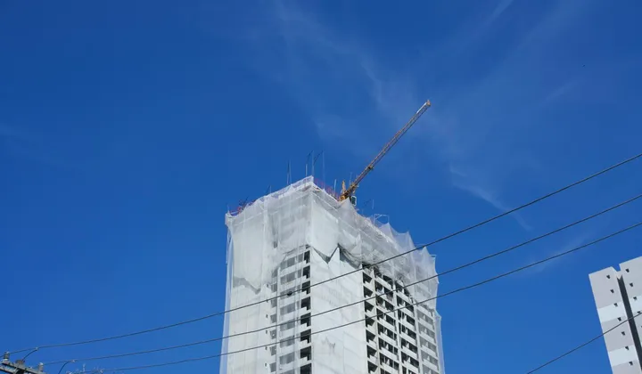 Edifício em construção com uma grua sob o céu azul.