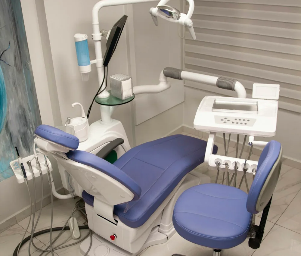 Consultório odontológico com cadeira azul e instrumentos de atendimento.