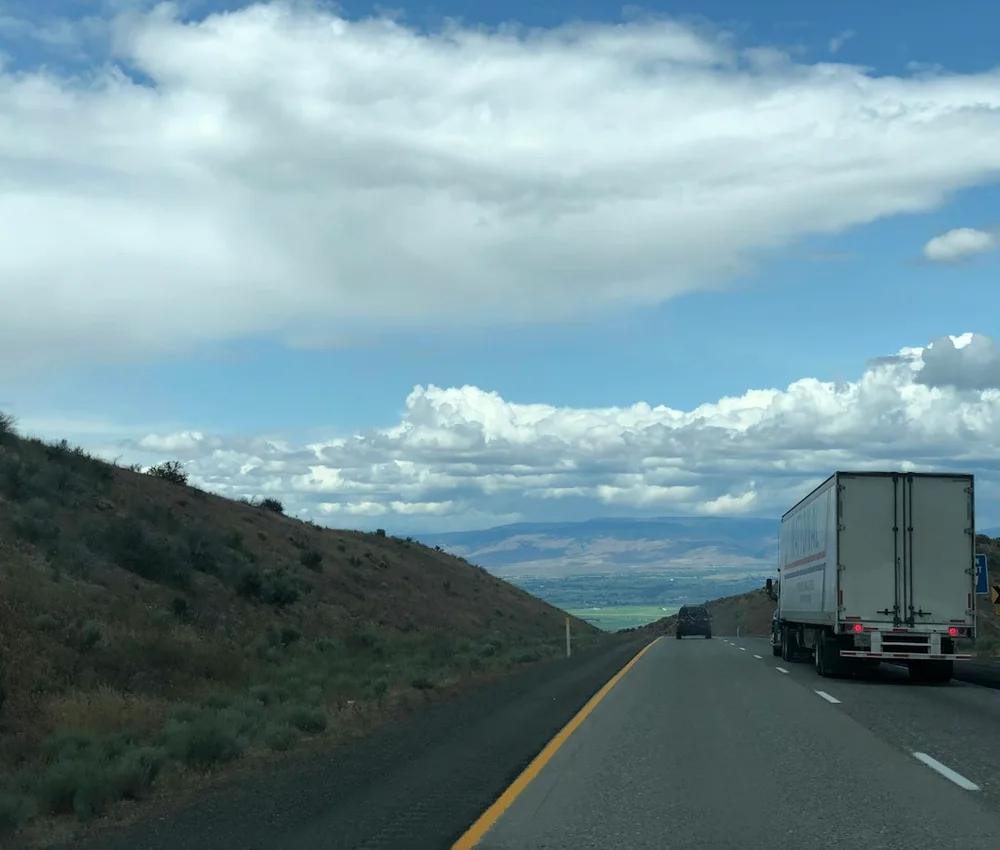 Caminhão de carga seguindo por uma rodovia entre colinas.
