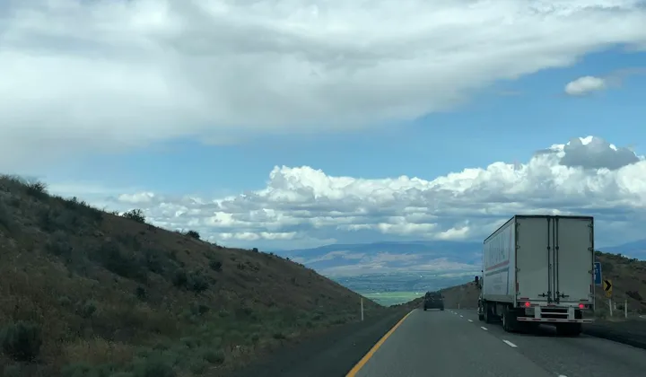 Caminhão de carga seguindo por uma rodovia entre colinas.