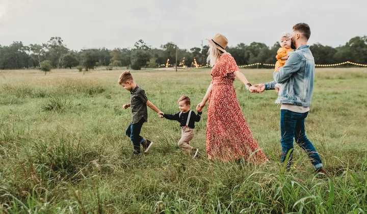 Família com crianças caminhando de mãos dadas em um campo.