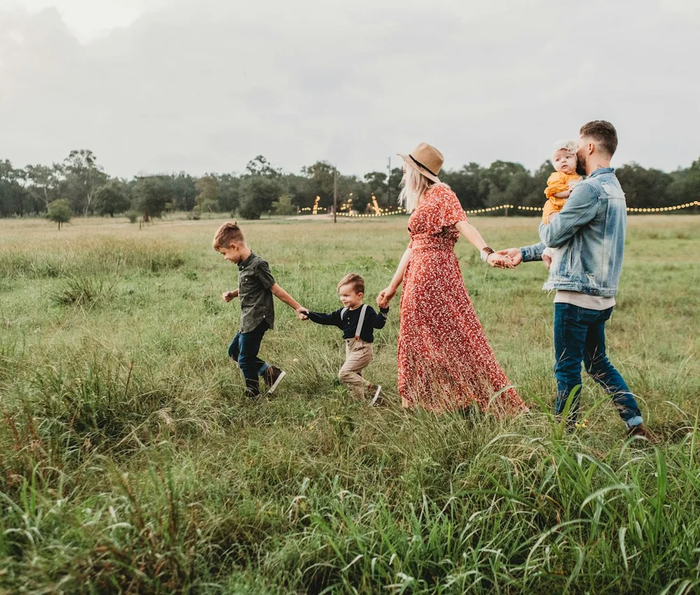 Família com crianças caminhando de mãos dadas em um campo.